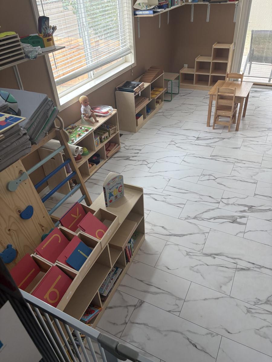 The classroom with low wooden shelves of materials along the wall, child-sized tables and chairs, and daylight coming through a large window
