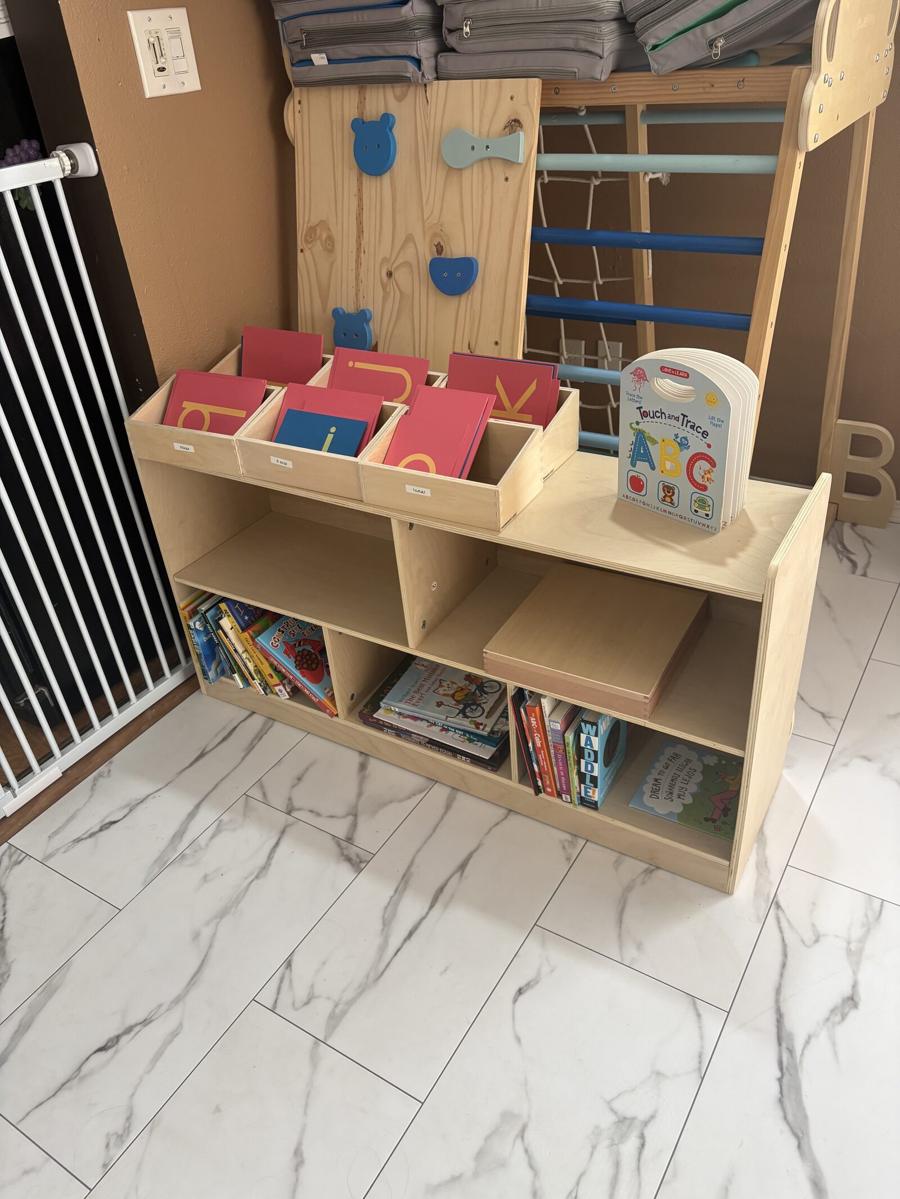 A language shelf with red and blue letter boxes in pull-out trays above open shelves of picture books