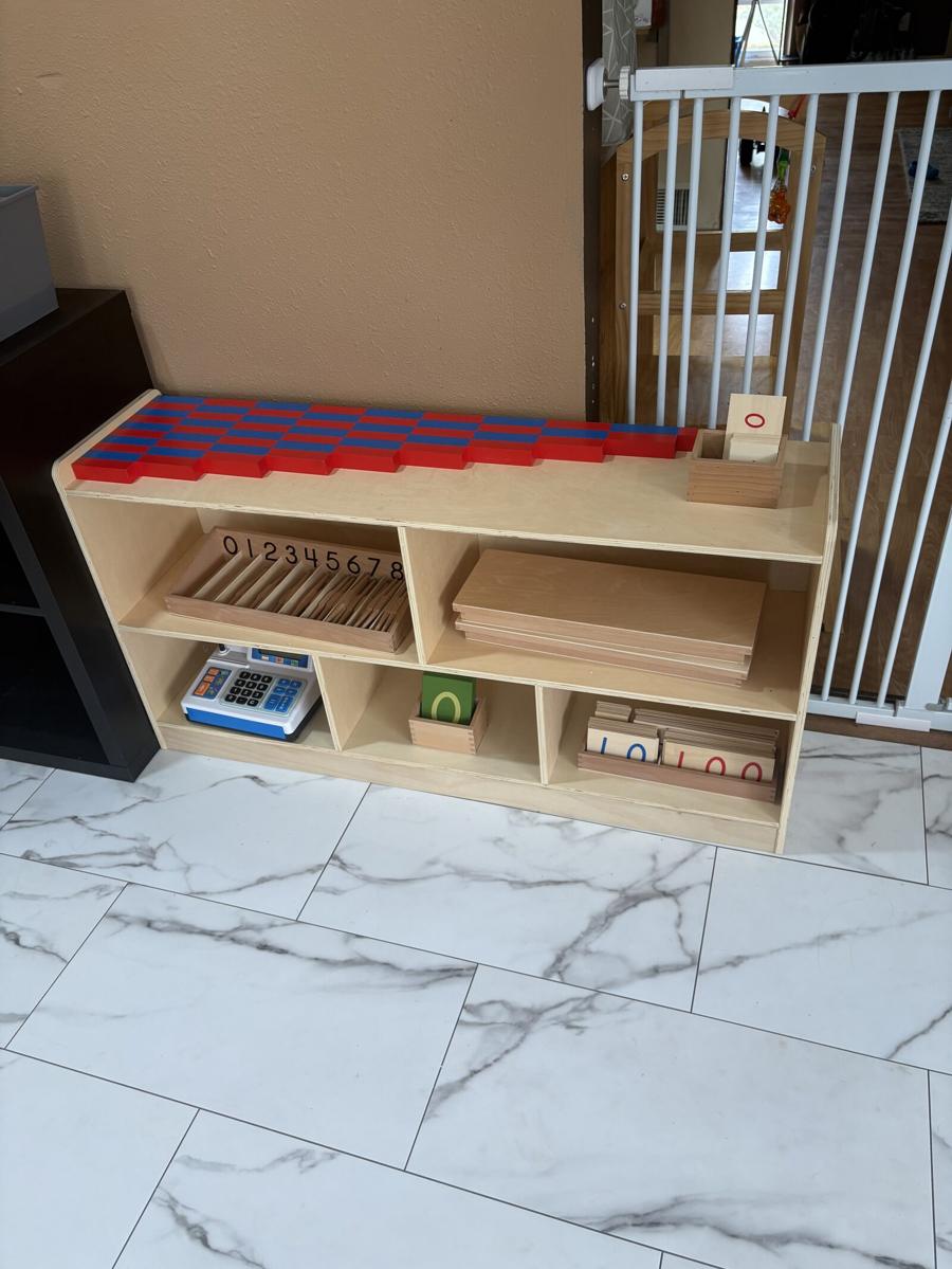 A math shelf with number rods arranged across the top and numeral strips, number cards, and counting materials on the shelves below