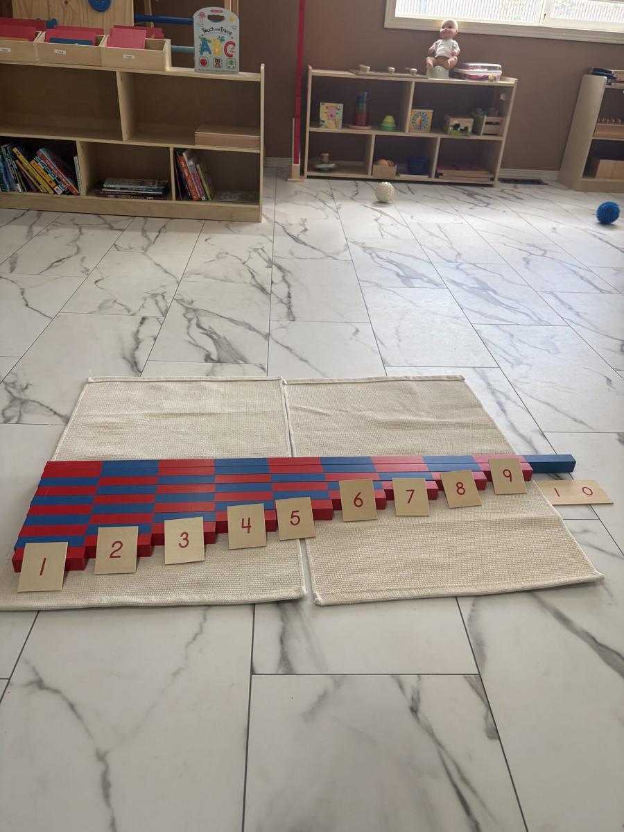 Montessori number rods laid out on a mat in order of length, each paired with a wooden numeral card from one to ten