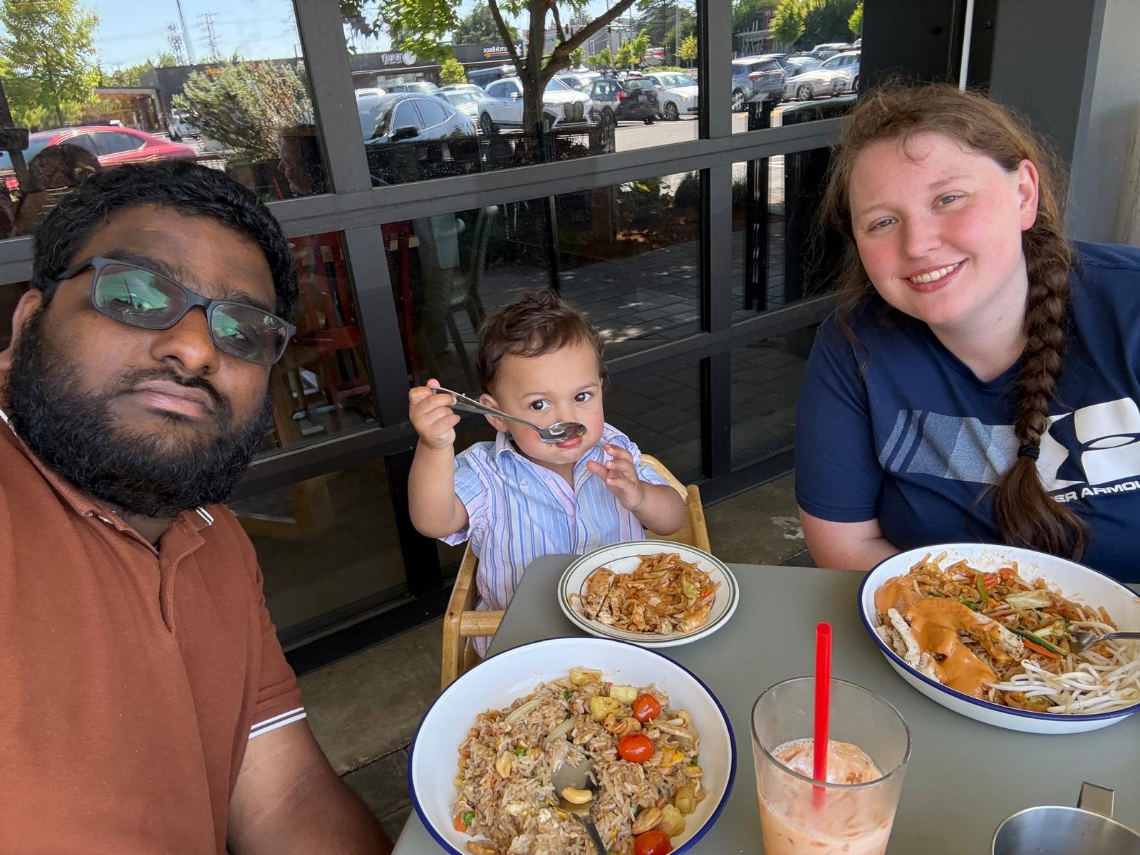 Miranda's family sharing a meal together at a table, with her one-year-old self-feeding with a spoon